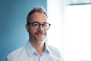 Smiling businessman wearing eyeglasses at workplace - JOSEF06887