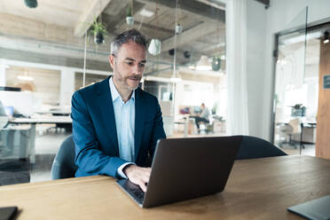 Selbstbewusster Geschäftsmann mit Laptop am Schreibtisch sitzend im Büro - JOSEF06892