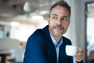 Thoughtful businessman holding coffee cup at office - JOSEF06901