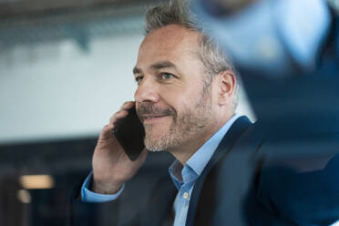 Smiling businessman talking on phone at workplace - JOSEF06913