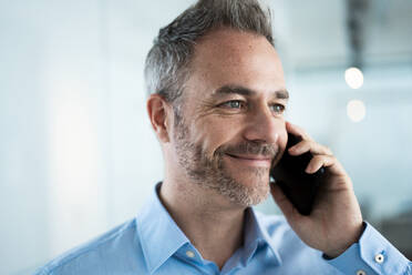 Smiling businessman talking on mobile phone in corridor - JOSEF06926