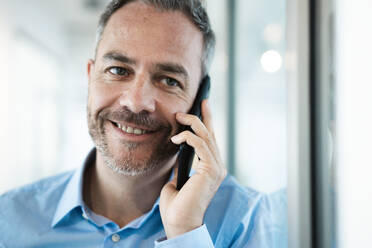 Smiling businessman talking on mobile phone in corridor - JOSEF06927