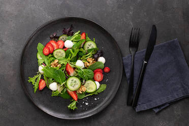 Dish with a summer salad of strawberries and cucumber on a dark table - ADSF33565