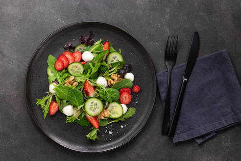 Gericht mit einem Sommersalat aus Erdbeeren und Gurken auf einem dunklen Tisch - ADSF33565