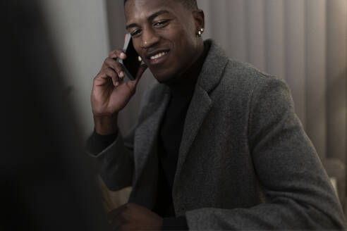 Lächelnder Geschäftsmann, der in seinem Büro zu Hause mit seinem Handy telefoniert und bis spät in die Nacht arbeitet - JPTF01038