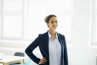 Businesswoman with hand on hip smiling at office - GUSF06726