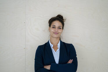 Businesswoman with arms crossed smiling in front of wall - GUSF06732