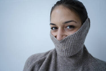 Verspielte Frau, die ihr Gesicht mit einem grauen Pullover vor einer Wand versteckt - GUSF06745