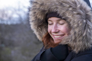 Junge Frau im Pelzmantel mit Kapuze lächelt mit geschlossenen Augen - LBF03619