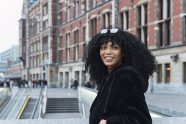 Smiling young curly haired woman looking over shoulder in city - PNAF02950