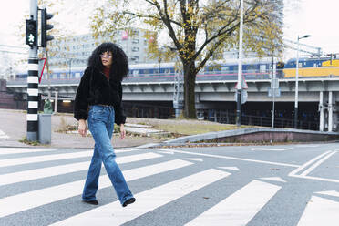 Fashionable woman crossing street on road marking in city - PNAF02971