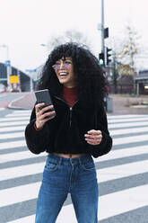 Glückliche junge Frau mit Smartphone auf einer Straßenmarkierung stehend - PNAF02972