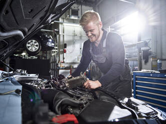 Lächelnder blonder Mechaniker, der einen Automotor in einer Autowerkstatt repariert - CVF01882