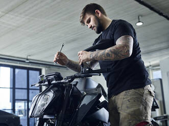 Tätowierter Mechaniker mit Werkzeug, der in einer Werkstatt an einem Motorrad arbeitet - CVF01886