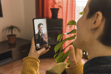 Smiling psychologist waving to patient on video call through smart phone at home - MGRF00616