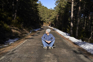 Man wearing knit hat sitting on skateboard - VEGF05281