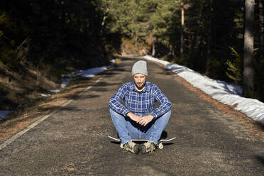 Man sitting on skateboard on sunny day - VEGF05282