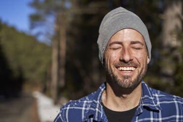 Happy man with eyes closed wearing knit hat on sunny day - VEGF05289