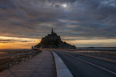 France, Normandy, Cloudy sky over bridge connecting Mont-Saint-Michel island at dusk - RUEF03507