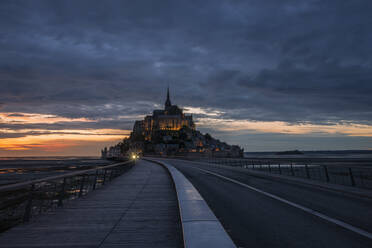 France, Normandy, Cloudy sky over bridge connecting Mont-Saint-Michel island at dusk - RUEF03508