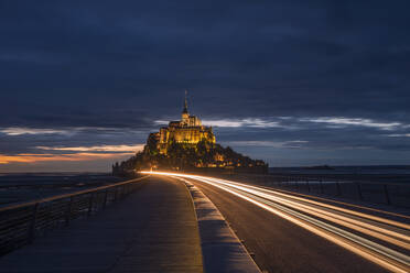 France, Normandy, Vehicle light trails stretching along bridge connecting Mont-Saint-Michel island at dusk - RUEF03509