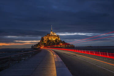 France, Normandy, Vehicle light trails stretching along bridge connecting Mont-Saint-Michel island at dusk - RUEF03511