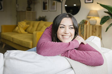 Happy beautiful woman leaning on sofa at home - XLGF02579