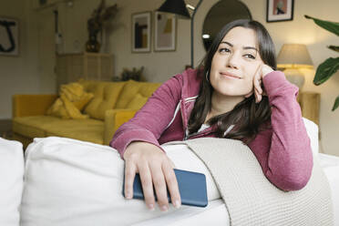 Thoughtful woman with smart phone sitting on sofa in living room - XLGF02582