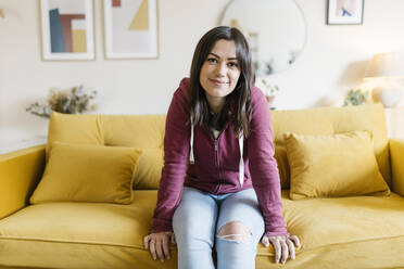 Lächelnde junge Frau sitzt auf dem Sofa im Wohnzimmer - XLGF02585