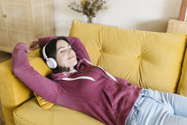 Smiling young woman with eyes closed relaxing on sofa at home - XLGF02588