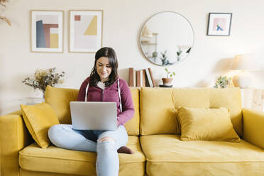 Junge Frau mit Laptop auf dem Sofa im Wohnzimmer sitzend - XLGF02594