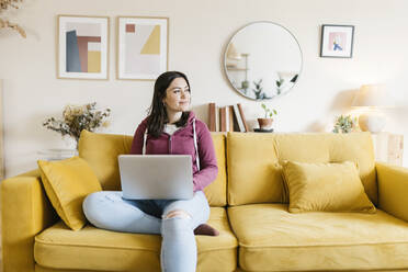 Frau mit Laptop sitzt zu Hause auf dem Sofa - XLGF02595