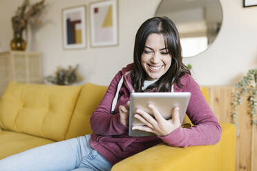 Glückliche Frau mit Tablet-PC auf dem Sofa zu Hause - XLGF02604