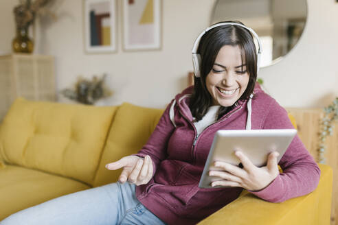 Glückliche Frau gestikuliert bei einem Videoanruf über einen Tablet-PC im Wohnzimmer - XLGF02607