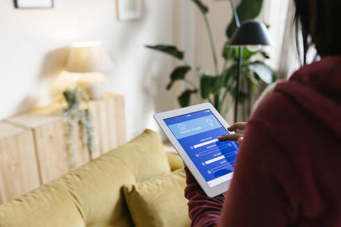 Junge Frau, die zu Hause die Beleuchtungsanlage über einen Tablet-PC einstellt - XLGF02611