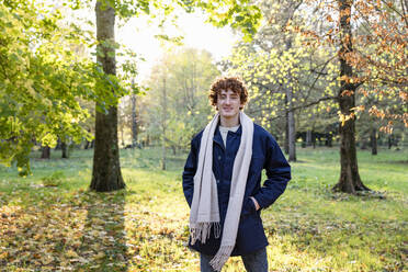 Junger Mann mit lockigem rotem Haar und Schal im Herbstpark stehend - EIF03271