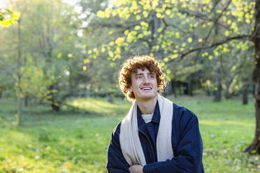 Glücklicher junger Mann mit roten Locken und Schal im herbstlichen Park - EIF03274