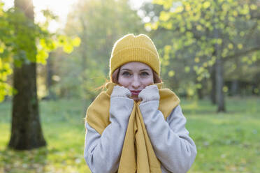 Smiling woman wearing yellow knit hat and scarf in autumn park - EIF03278