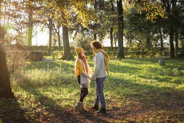 Lächelndes Paar, das sich an den Händen hält und im Herbst im Park steht - EIF03286