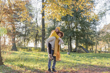 Junger Mann nimmt seine Freundin im Herbst im Park huckepack - EIF03288
