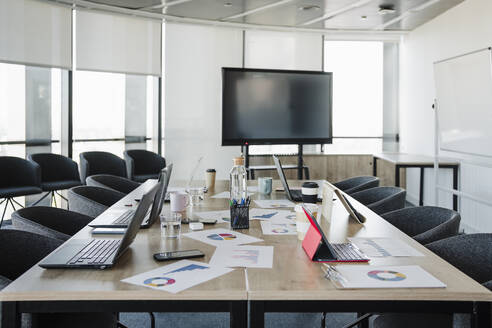 Laptops and graphs kept on conference table in empty meeting room - EBBF05265