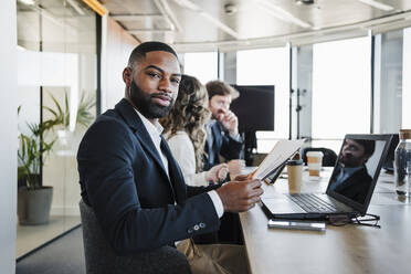 Young businessman sitting with documents and laptop at desk - EBBF05282