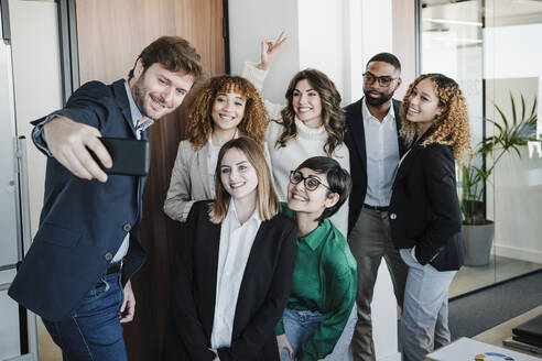 Smiling businessman taking selfie with colleagues through smart phone in office - EBBF05327