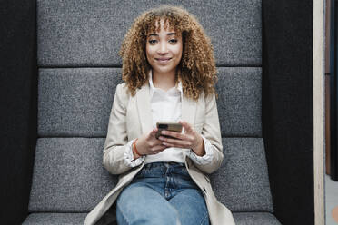 Smiling businesswoman with mobile phone sitting in office - EBBF05363