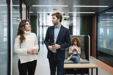 Businesswoman discussing with businessman standing in corridor - EBBF05365