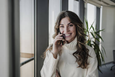 Arbeitende Frau, die im Büro mit ihrem Smartphone telefoniert - EBBF05386