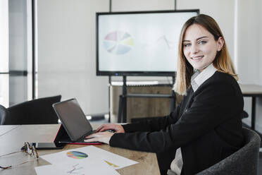 Lächelnde junge Geschäftsfrau mit Tablet-PC am Schreibtisch im Büro sitzend - EBBF05409