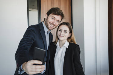 Geschäftsmann und Geschäftsfrau nehmen Selfie durch Handy im Büro - EBBF05418