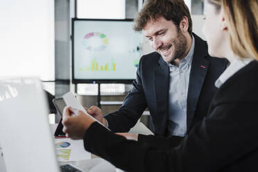 Smiling businessman discussing report with colleague in office - EBBF05428