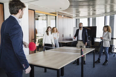 Business colleagues playing table tennis in coworking office - EBBF05440